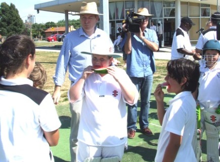 Under 12s player Riley Boxshall tucks into our healthy watermelon with teammates while Victoria's Health Minister David Davis and the media look on.
